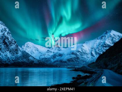 Northern lights over the snowy mountains, frozen sea, reflection in water at winter night in Lofoten, Norway. Aurora borealis and snowy rocks. Landsca Stock Photo