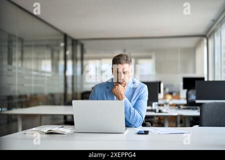 Serious busy middle aged professional business man using laptop in office. Stock Photo