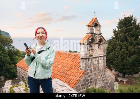 A young woman tourist exploring a monastery in Montenegro, using a smartphone app for navigation. Stock Photo