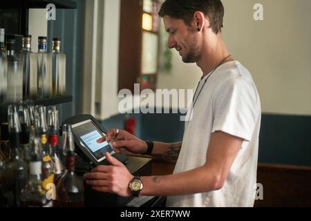 Young man, bartender and order with pos system for receipt, checkout or register in liquor store. Male person or happy barman working on tablet screen Stock Photo