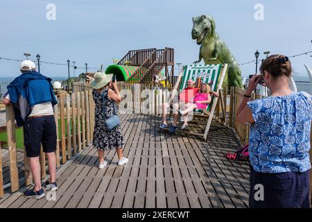 Visitors pose for a holiday snap sitting on a giant deckchair, Paignton Pier, Devon Stock Photo