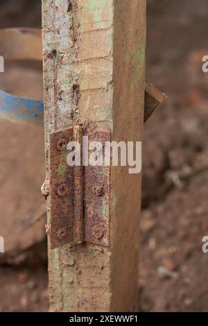 close-up of old rusty metal hinge on wooden pole, reddish brown iron oxide corrodes exposed to moisture and dirt outdoor, blurry background Stock Photo