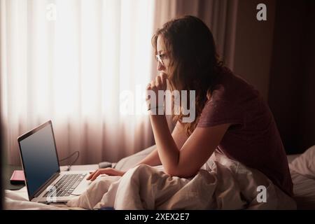 Laptop, morning and woman in bedroom for networking on internet, social media or website. Technology, glasses and female computer engineer doing Stock Photo