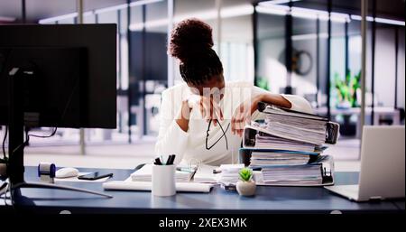 Overworked Businesswoman Struggles with Tax Calculations at Desk in Corporate Office, feeling tired and frustrated with paperwork stacks. Stock Photo