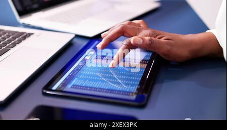 Analyzing Financial Charts on a Tablet in the Workplace: An African American Data Analyst Reports on Virtual Accounts. Stock Photo