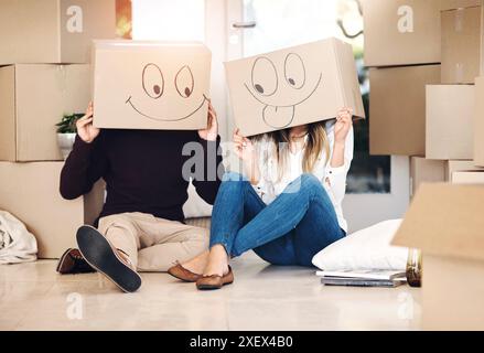 New home, box and couple with emoji on floor for property, moving day and mortgage. Homeowner, real estate and man and woman with funny face drawing Stock Photo