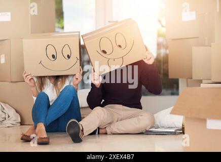 New home, box and couple with emoji face on floor for property, moving day and mortgage. Homeowner, real estate and man and woman with funny drawing Stock Photo