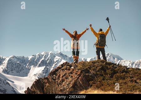 Two young happy successful hikers are standing in winner pose high in mountains against glaciers and blue sky Stock Photo