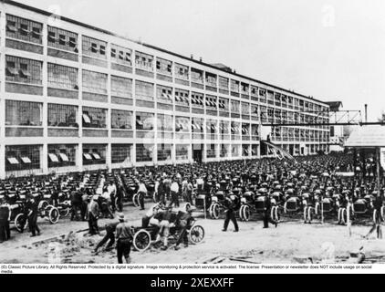 Ford history. It's factory in Highland park Michigan USA was a production facility for the Model T car and has become known for being the first factory in history to assemble cars on a moving assembly line. Picture shows the factory building and chassis in mass outside it.  1913 Stock Photo