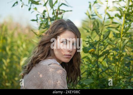 Nice healthy young model woman with clean fresh skin, natural make-up and curly hairstyle against green grass background, outdoor portrait Stock Photo