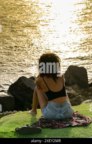 Miami, Florida, USA - 5 December 2023: Person siiting on the waterfront looking at the setting sun reflecting on the sea Stock Photo