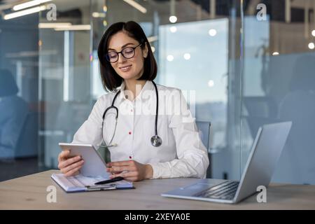 Female doctor using tablet computer at office . Modern medical professional wearing stethoscope, working with technology at workplace. Confident, focused healthcare provider reviewing information. Stock Photo