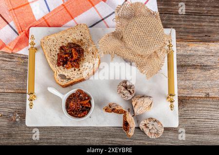 Flat composition with delicious fig jam on wooden table. Delicious fig jam in a glass jar on a marble tray and fig jam spread on bread, lying flat. Stock Photo