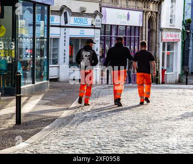 Three workers in high visibility orange trousers walking on a cobblestone street in Falmouth Cornwall UK Stock Photo
