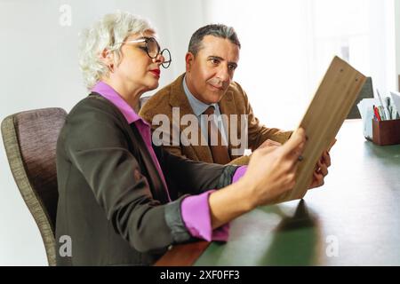 Corporate professionals or married couple discussing and reviewing documents with a notary in an office setting. Business partners collaborating on st Stock Photo