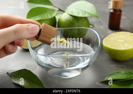 Woman dripping essential oil from pipette into bowl at gray table, closeup Stock Photo