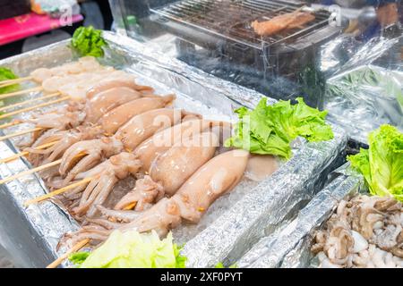 Thai strret food on night market. Skewered raw squids displayed on bed of ice, ready to be grilled. Asian food in Bangkok, Thailand Stock Photo