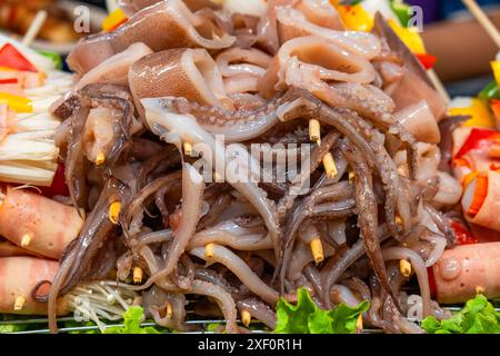 Skewered raw octopuses and squids ready to be grilled. Thai strret food on night market. Asian food in Bangkok, Thailand Stock Photo