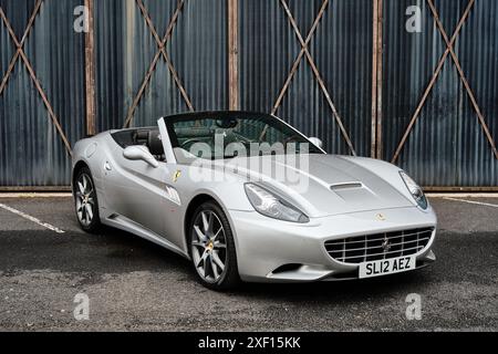 Silver Ferrari California convertible car with its roof down outdoors isolated against a plain warehouse background with copy space Stock Photo