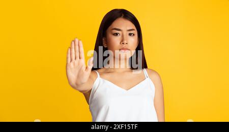 Young Woman Makes Stop Gesture Against Yellow Background Stock Photo