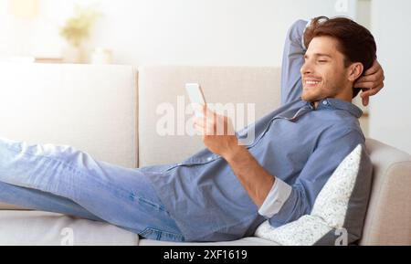 Man Relaxing on Couch Using Smartphone Stock Photo