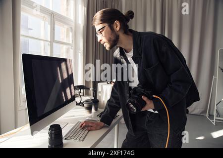 Minimal side view portrait of bearded young man as professional photographer using computer in studio with sunlight accent, copy space Stock Photo