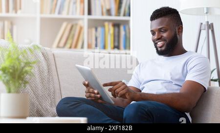 Happy Man Using Tablet While Relaxing on a Couch Stock Photo