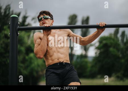 Fit man doing pull ups outdoors at an outdoor gym for strength training Stock Photo