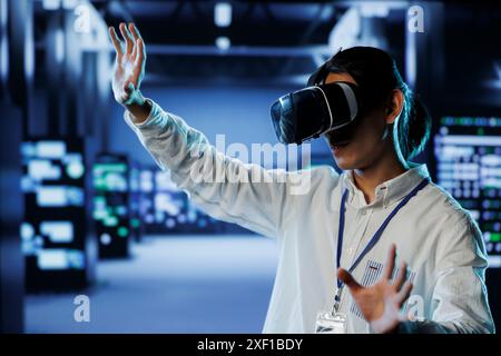 Certified developer in data center uses virtual reality to prevent system overload. Expert with VR goggles in server farm ensuring enough network bandwidth for smooth operations Stock Photo