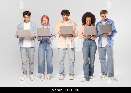 Five Diverse Young Adults Using Laptops in Studio Setting Stock Photo