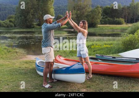 Happy young couple at canoe ride giving high five on a beautiful green lake Stock Photo