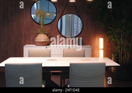 A large white table with two chairs and a vase of flowers in the center. The room is well lit and has a modern, minimalist design Stock Photo