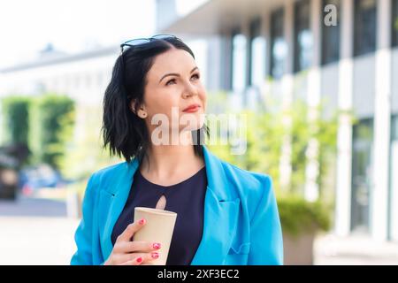 Young elegant Asian professional business woman, lady executive manager wearing suit holding coffee cup standing outdoor during work break.  Stock Photo
