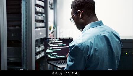 Server room, black man or coding with laptop for system upgrade, cybersecurity or screen. Software management, data or male programmer with digital Stock Photo