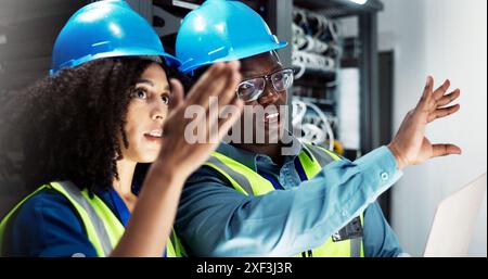 Team, engineers and communication in server room for support, repairs and equipment by laptop. Man, woman and together with PPE for cybersecurity Stock Photo