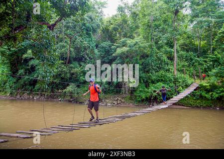 Thailand, Chiang Mai  province; Boy walks on a wooden suspension bridge that crosses a river in the rainforest. Stock Photo