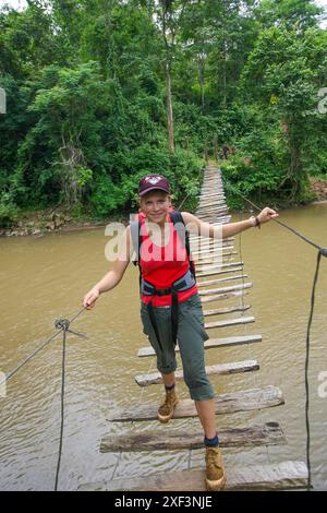 Thailand, Chiang Mai  province; Boy walk on a wooden suspension bridge that crosses a river in the rainforest. Stock Photo