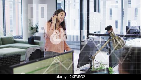 Image of icons, graphs, map, computer language, caucasian female talking on imagecall in office Stock Photo