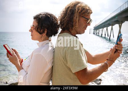 couple on the beach browsing smartphones apps. Stock Photo