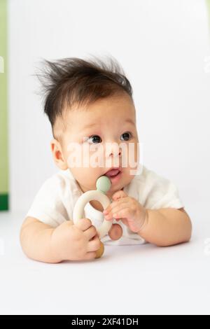 The baby boy is learning to crawl and playing with gum, white clothes and lying on the white floor, black hair, baby playing and posing in different u Stock Photo