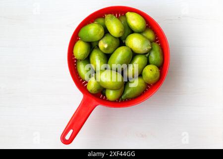 Fresh green lemons in plastic red basket on light wooden background. Top view. Stock Photo