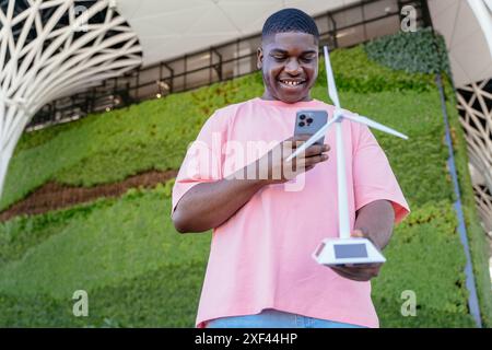 A man in a pink shirt is holding a cell phone and looking at a wind turbine Stock Photo