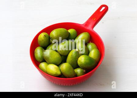 Fresh green lemons in red basket on light wooden background. Stock Photo