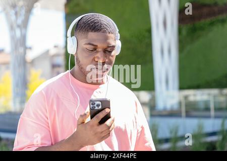 A man wearing a pink shirt is looking at his cell phone while wearing headphones Stock Photo
