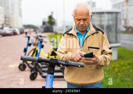 Old man using smartphone to activate e-scooter Stock Photo
