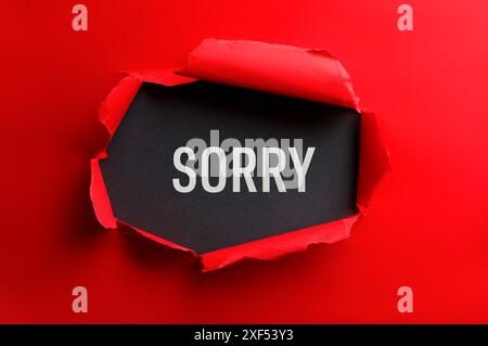 Word Sorry on black background, view through torn red paper Stock Photo