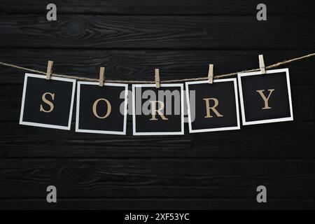 Word Sorry made of paper notes with letters hanging on rope against black wooden background Stock Photo