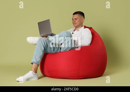 Handsome man with laptop on red bean bag chair against green background Stock Photo