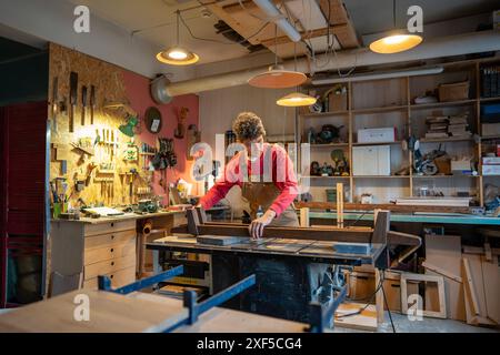 Concentrated man carefully working in carpentry creative studio, engaged in creation of bed. Stock Photo