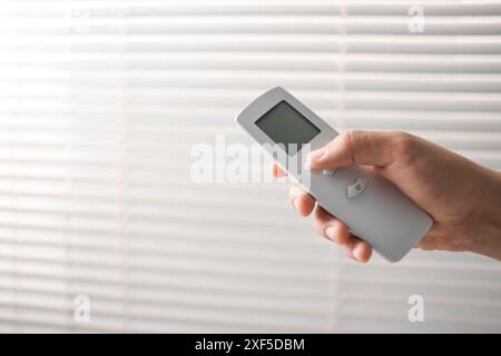 Man using remote control to adjust window blinds indoors, closeup. Space for text Stock Photo